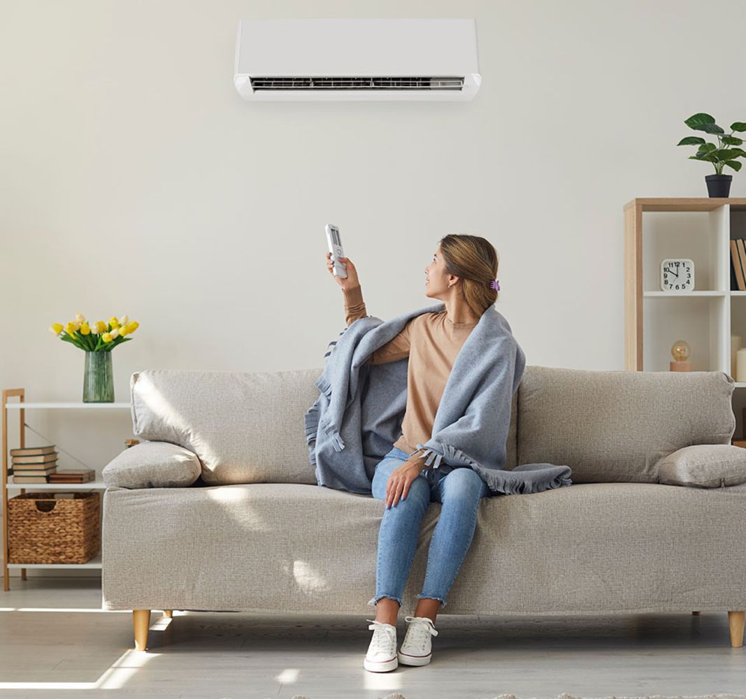 Eine Frau sitzt auf dem Sofa und bedient eine Klimaanlage, die sich hinter ihr befindet, mit einer Fernbedienung